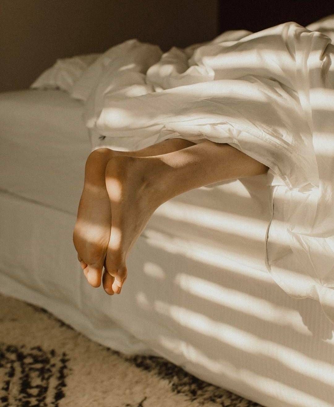Feet resting under soft linen sheets in morning light